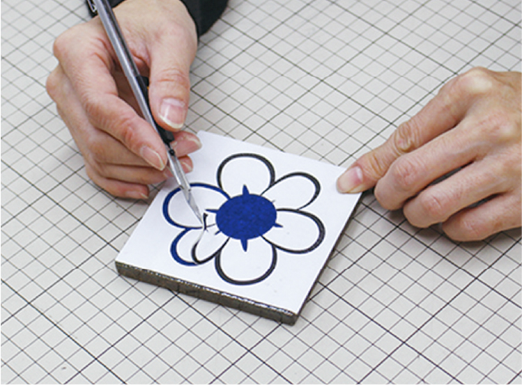 A rubber mask is applied to the tile, and after cutting along the design, only the areas to be ground are removed.